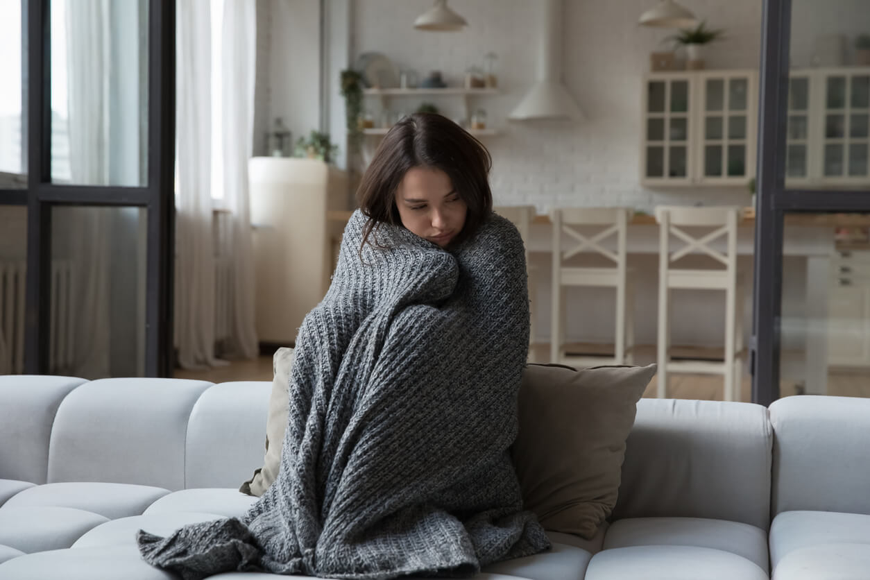 Unhappy girl wrapped in a blanket due to the house being cold